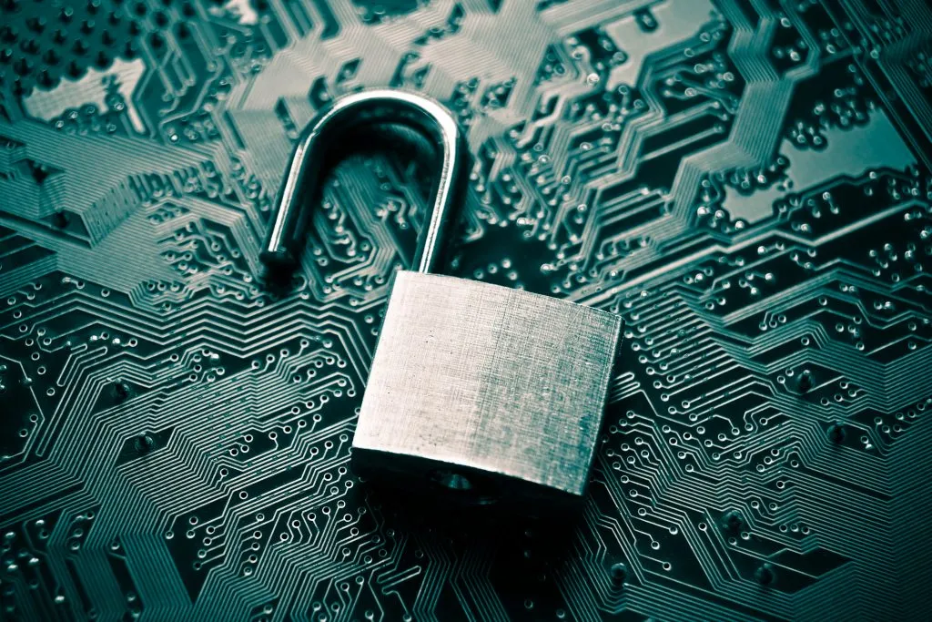 A silver open padlock resting on a dark teal/blue circuit board, symbolizing data security or a breach