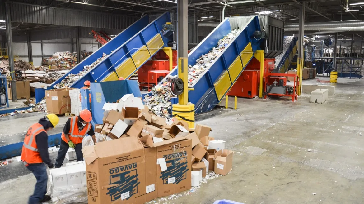 A team of workers is seen loading boxes onto a conveyor belt in an industrial environment.
