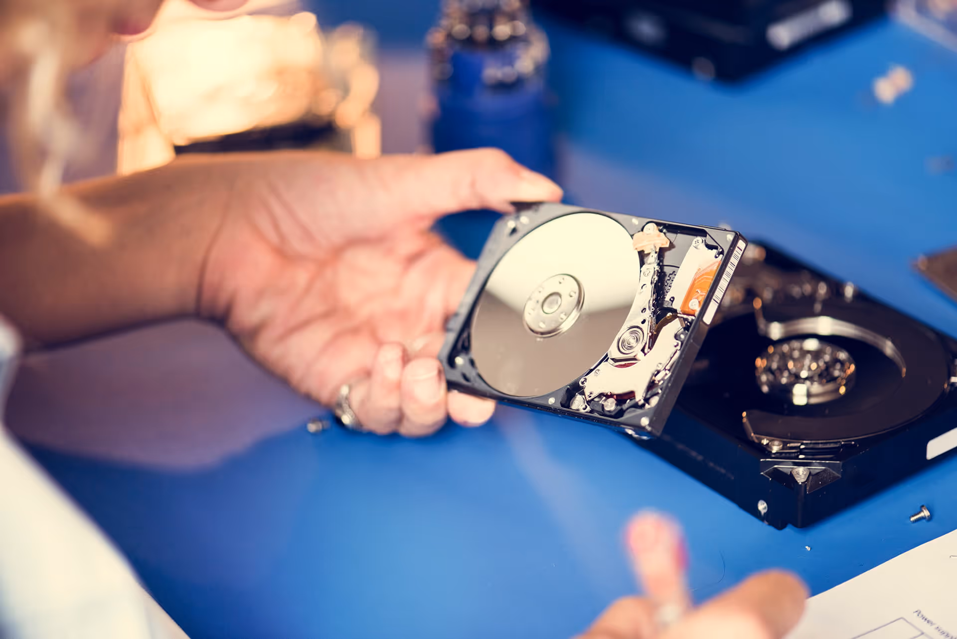 Technician holding an open hard disk drive (HDD) during a repair or data recovery process at a workshop