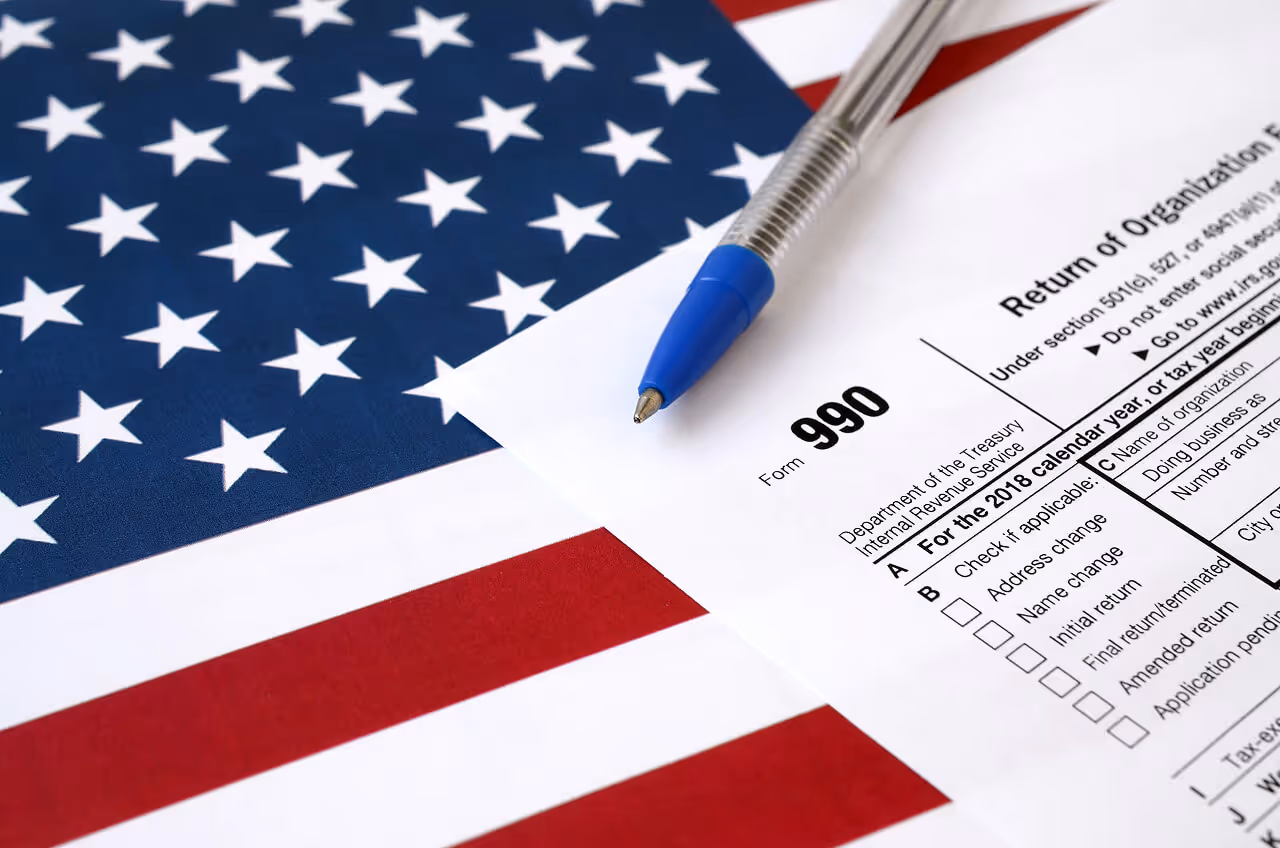 IRS Form 990 tax return for exempt organizations on a US flag with a pen