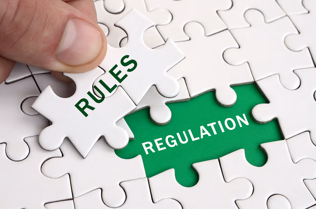 Hand placing a "Rules" puzzle piece into a gap revealing the word "Regulation" on a green background