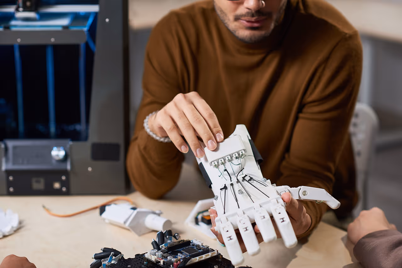 Engineer examining a 3D-printed robotic hand prototype in a lab with a 3D printer in the background