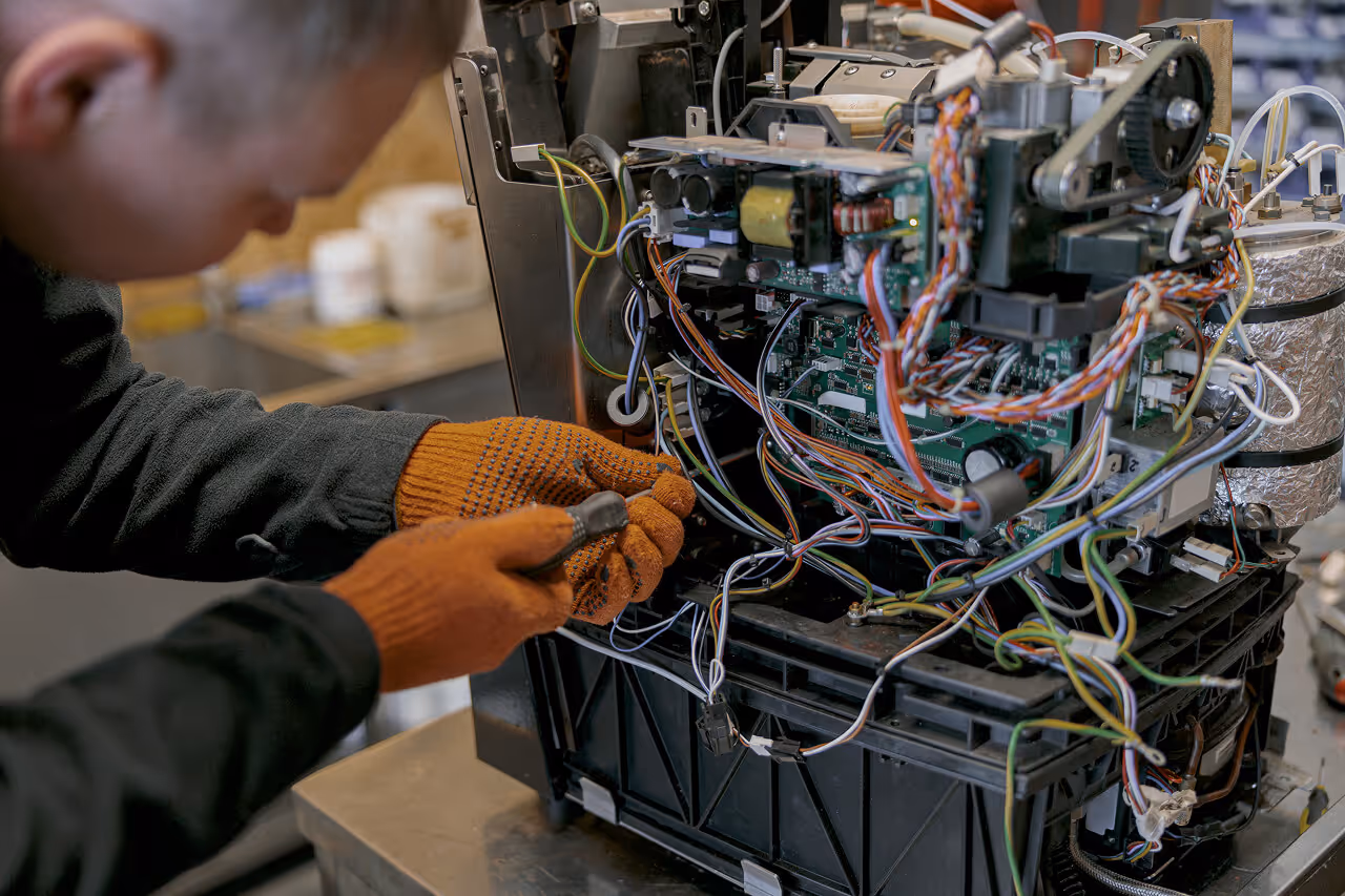 Technician using a screwdriver to repair the complex internal wiring and components of a coffee machine