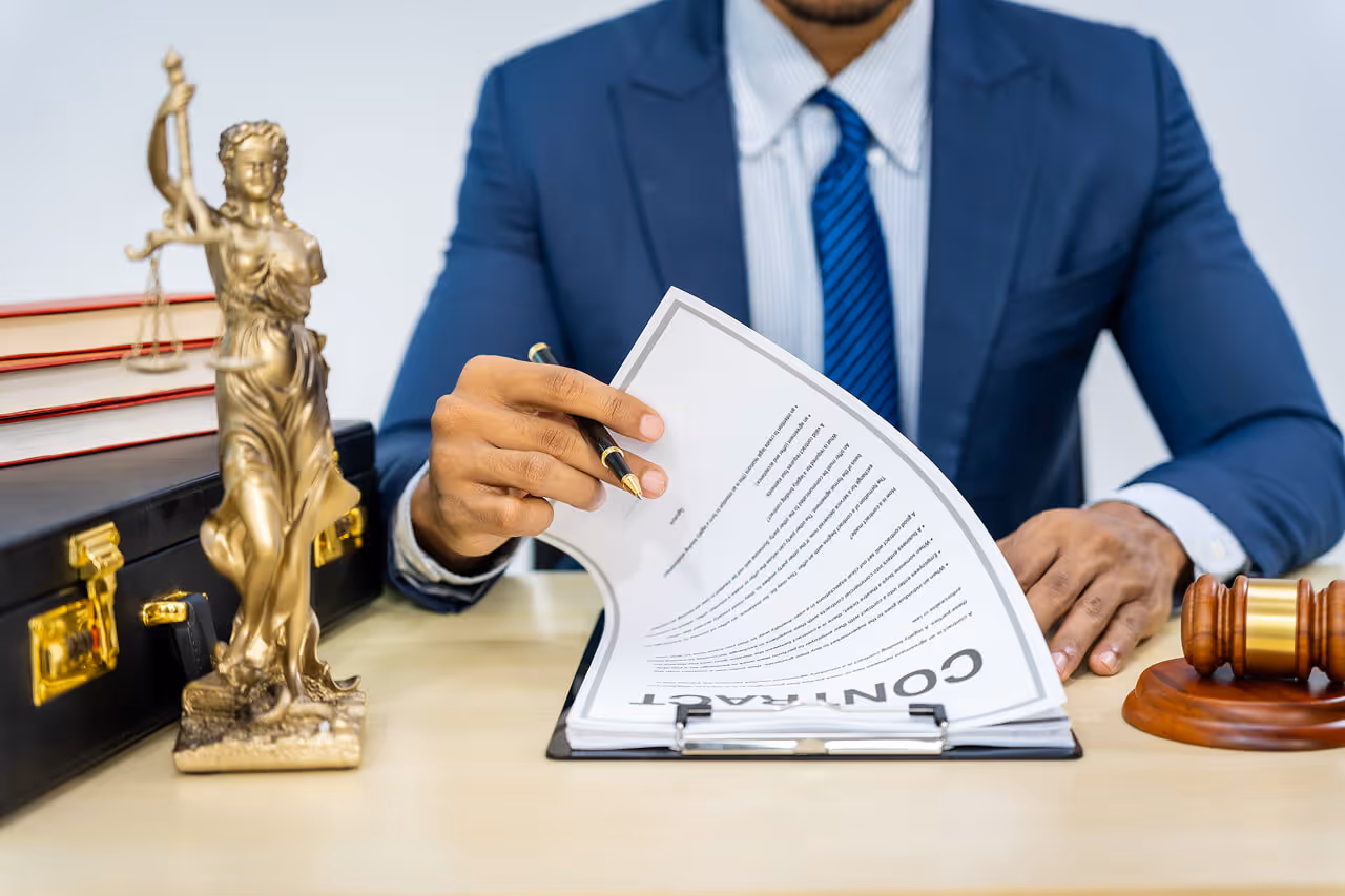 Lawyer in a suit reviewing a legal contract on a desk with a Lady Justice statue and gavel